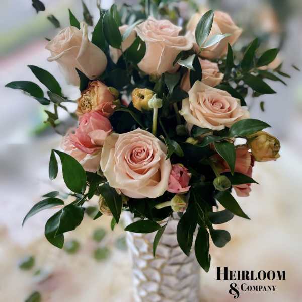 Blush roses arranged in a textured white vase with dark foliage