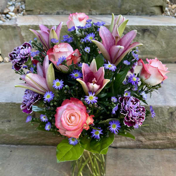 Pink roses, lilies, and purple daisies in a glass vase