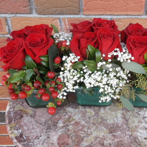 Red roses arranged in three small glass containers with white filler flowers