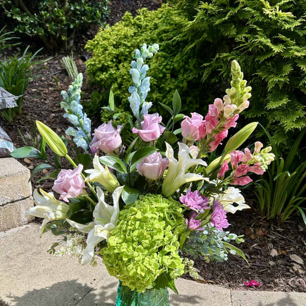 Mixed bouquet in a turquoise glass vase with lilies, roses, snapdragons, and hydrangea