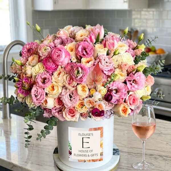 Large pink and cream floral arrangement in a white hat box beside a wine glass