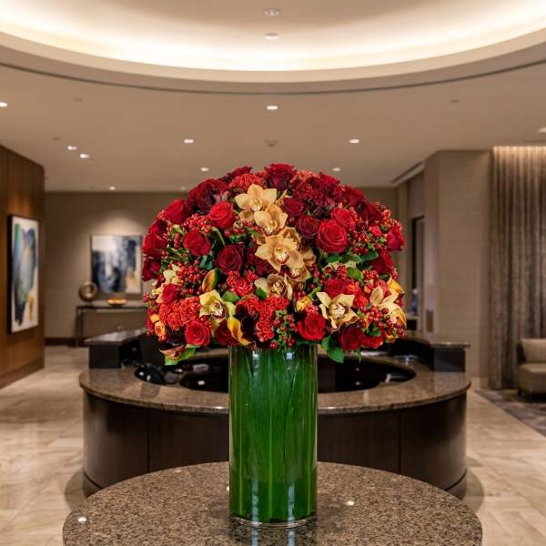 Large red and gold floral arrangement in a tall green glass vase