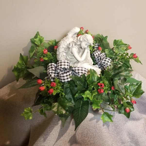 Angel figurine surrounded by red berry-like flowers and ivy with a plaid ribbon