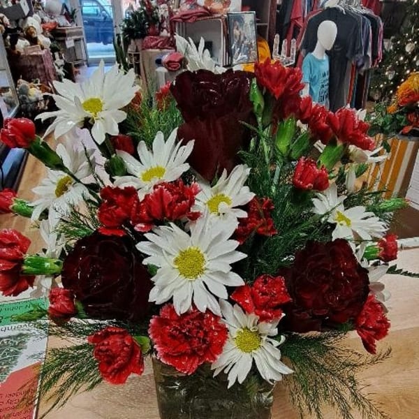 Red carnations and white daisies arranged in a square glass vase.