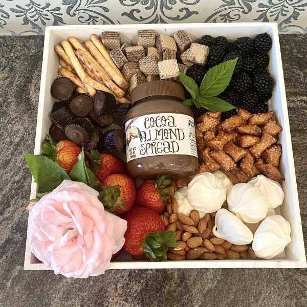 Gift tray with fruit, chocolates, crackers, nuts, and a pink rose