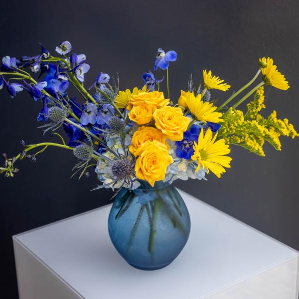 Blue and yellow flower arrangement in a blue glass vase