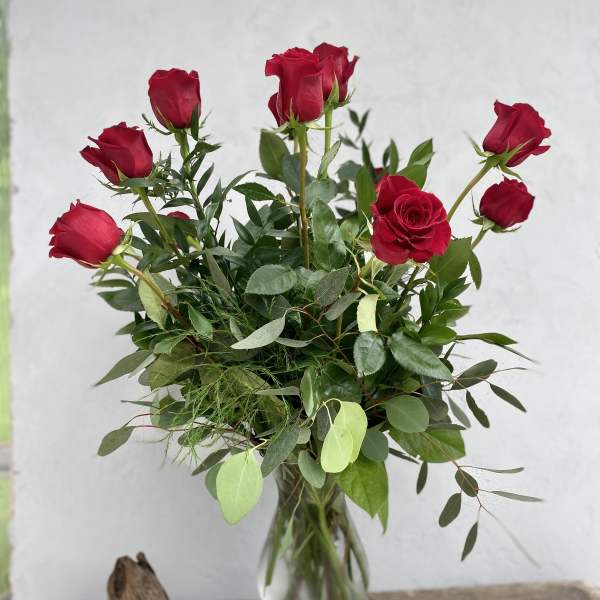 Red roses in a clear glass vase with mixed greenery