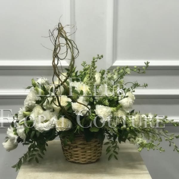 White floral arrangement in a woven basket with trailing greenery