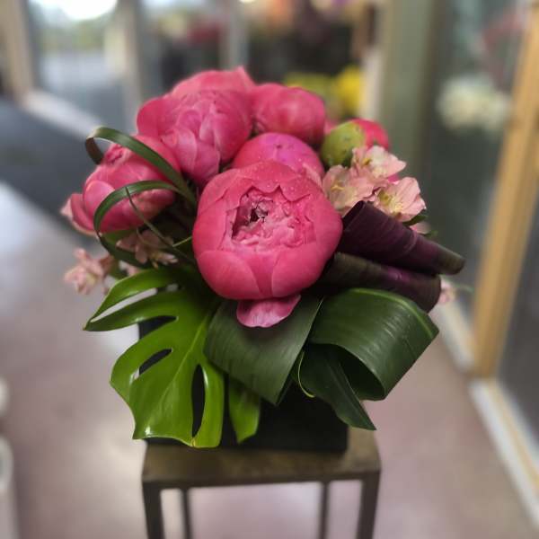 Pink peony bouquet with tropical leaves and small pale blossoms