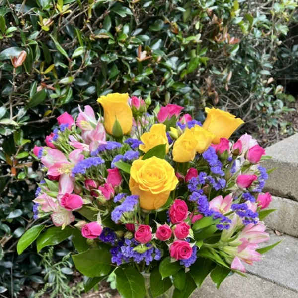 Bouquet of yellow roses, pink alstroemeria, and purple filler in a glass vase