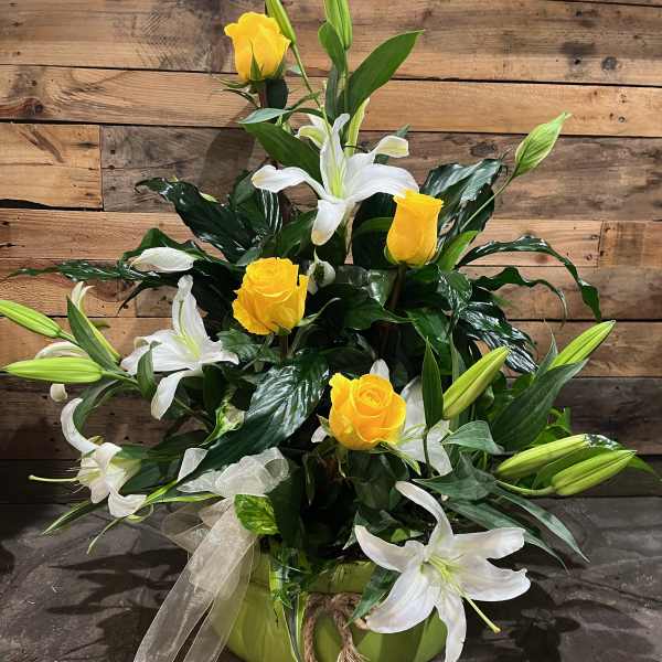 Yellow roses and white lilies arranged in a green vase with a ribbon bow.