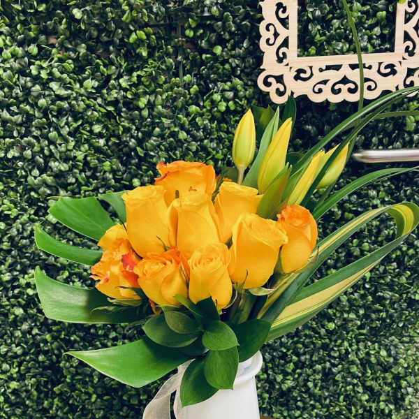 Yellow and orange roses in a white vase with a silver ribbon