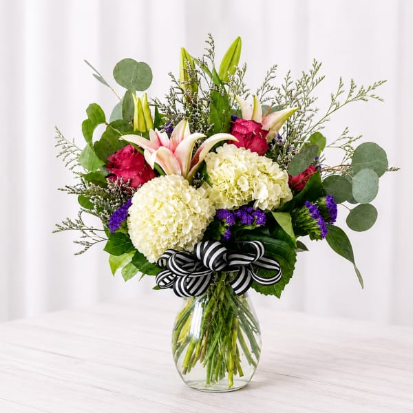 Bouquet of white hydrangeas, pink lilies, and roses in a glass vase