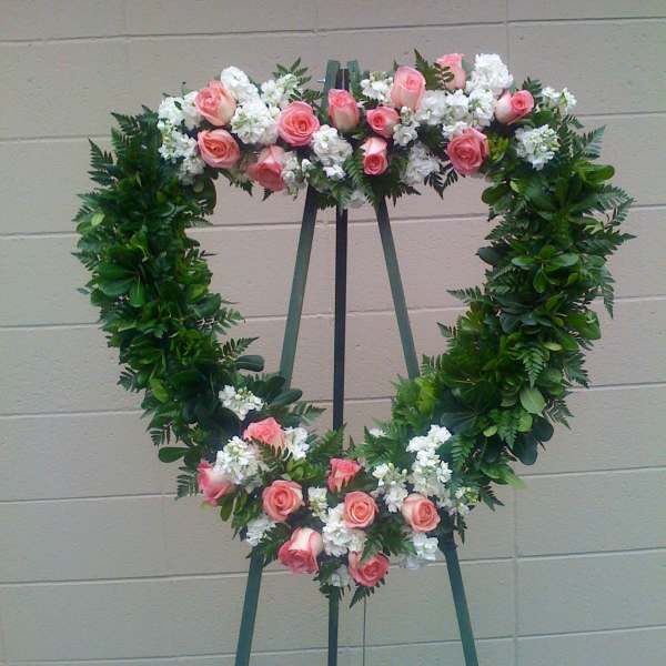 Heart-shaped floral wreath with pink roses and white flowers on an easel