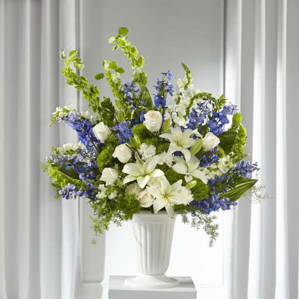 White lilies and roses arranged with blue flowers in a white vase.