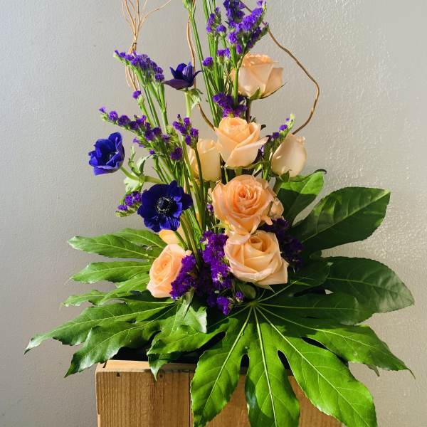 Tall bouquet of peach roses and purple flowers with large green leaves