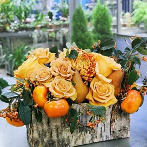 Yellow roses and orange fruit arranged in a rustic wooden box