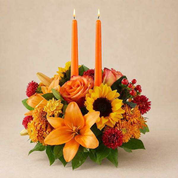 Orange floral centerpiece with two lit taper candles