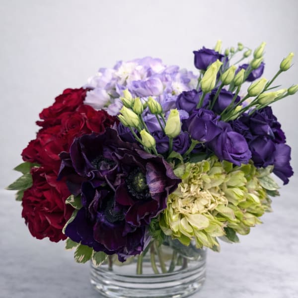 Mixed bouquet of purple, red, and green flowers in a clear glass vase