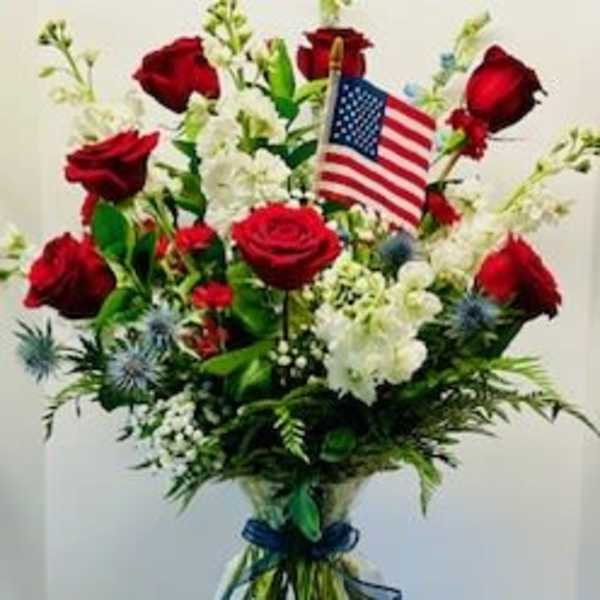 Red roses and white flowers in a clear vase with a small American flag
