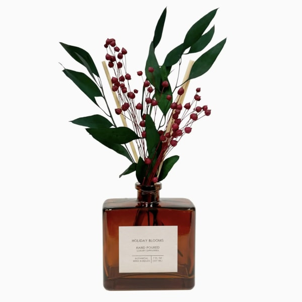 Amber reed diffuser bottle with red berry stems and green leaves