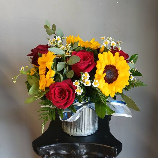 Bouquet of red roses, sunflowers, and small white daisies in a silver container