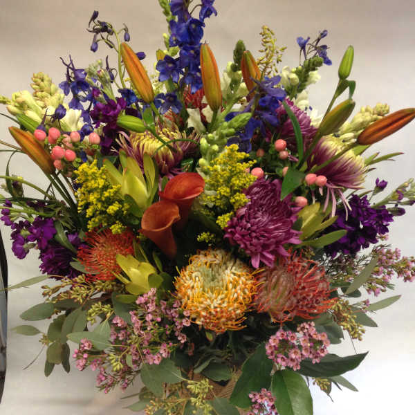 Mixed bouquet with lilies, calla lilies, and purple blooms in a burlap-wrapped vase