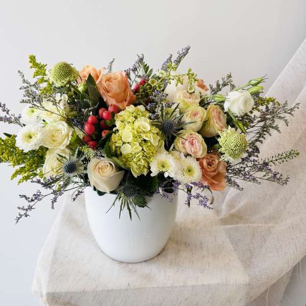 Mixed bouquet of peach, white, and green flowers in a white vase