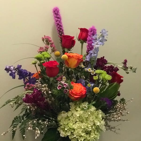 Tall mixed bouquet with roses, hydrangea, and purple accent flowers in a dark vase