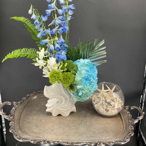 Blue and white floral arrangement in a white vase with green accents
