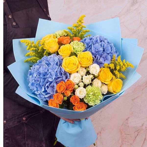 Bouquet of blue hydrangeas, yellow and orange roses, and green carnations in blue wrap