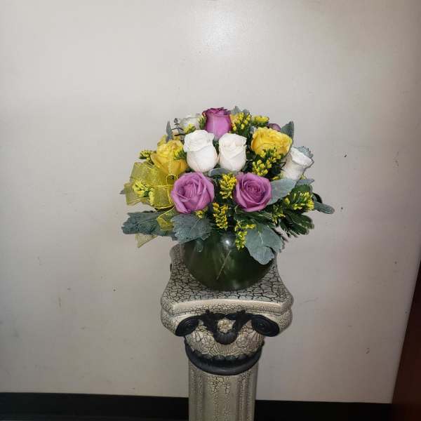 Bouquet of purple, white, and yellow roses in a dark vase