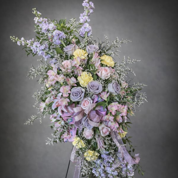 Large pastel floral standing spray with roses, lilies, and ribbons on an easel