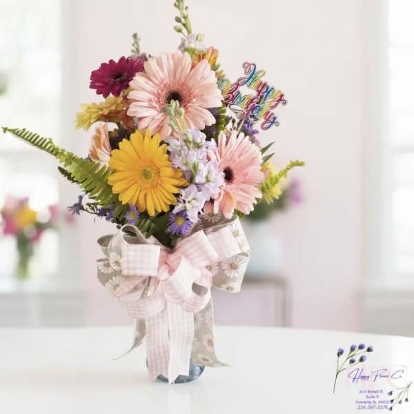 Mixed gerbera daisy bouquet in a glass vase with a pink ribbon