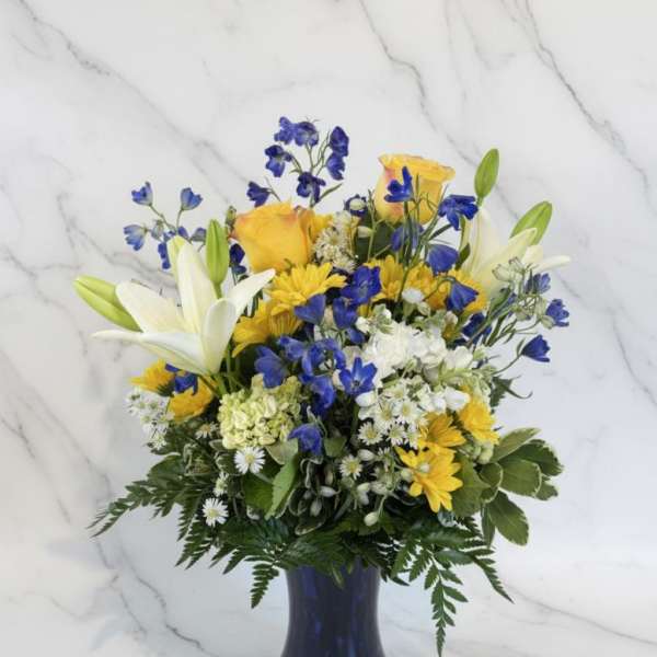 Blue and yellow mixed bouquet in a dark vase