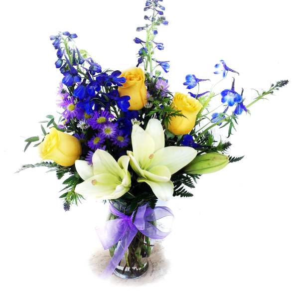 Bouquet of yellow roses, white lilies, and blue flowers in a glass vase