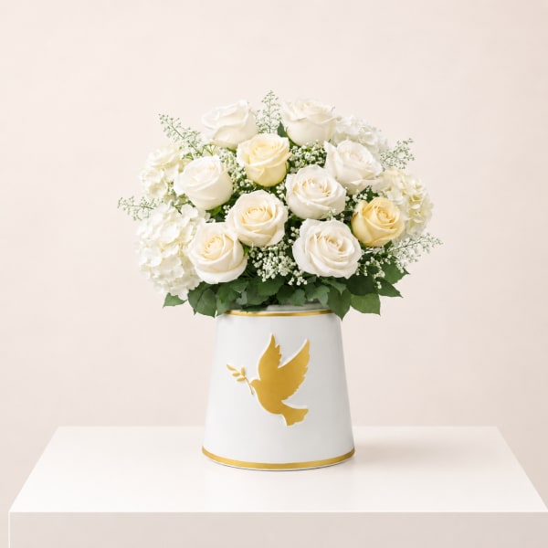 White roses and hydrangeas in a white vase with a gold dove design
