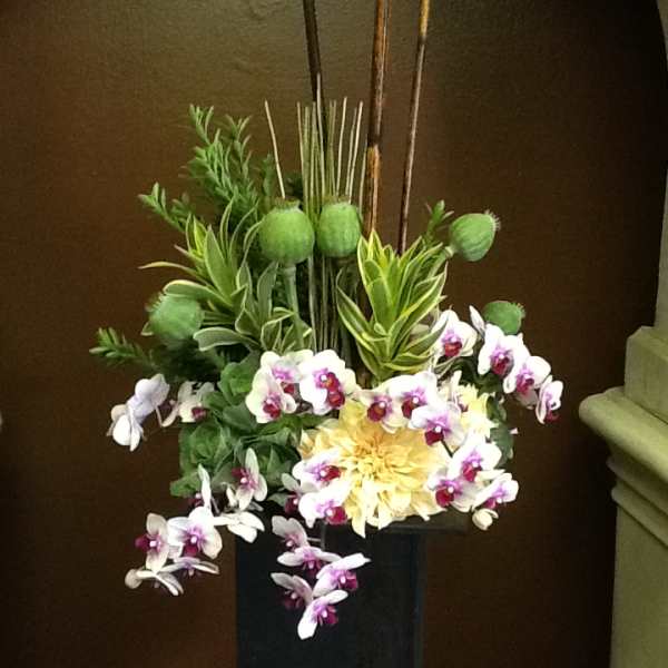 Tall floral arrangement with orchids and a yellow bloom in a black vase