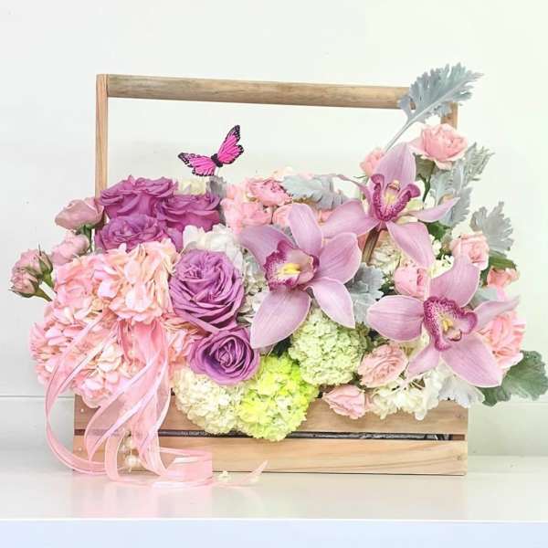 Pink and purple floral arrangement in a wooden box with orchids and roses