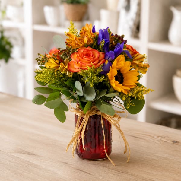 Colorful bouquet of roses, sunflowers, and purple blooms in a red glass vase