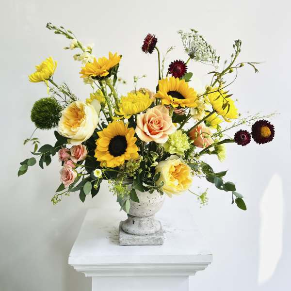 Mixed bouquet with sunflowers, roses, and yellow blooms in a gray pedestal vase