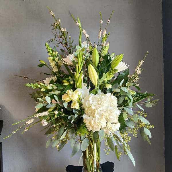 Tall white floral arrangement in a clear glass vase with lilies and hydrangea