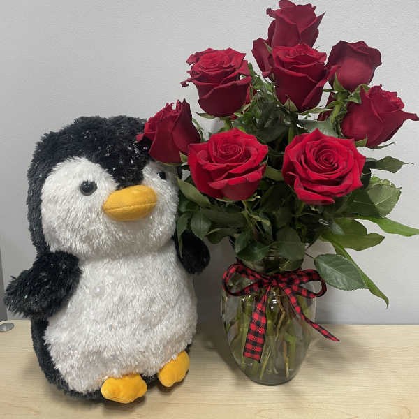 Red roses in a glass vase beside a plush penguin