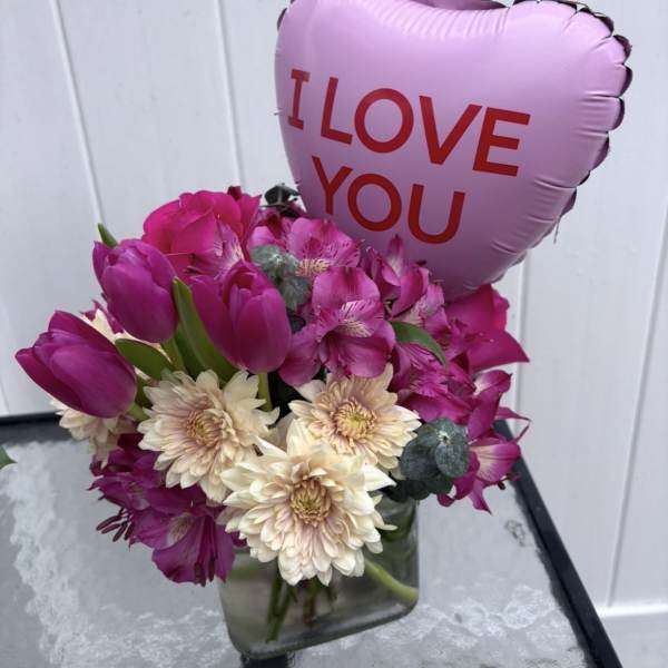 Pink bouquet with tulips and daisies in a glass vase, topped with a heart balloon