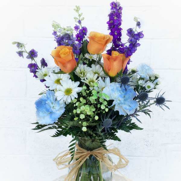 Bouquet of orange roses, blue carnations, and purple flowers in a glass vase