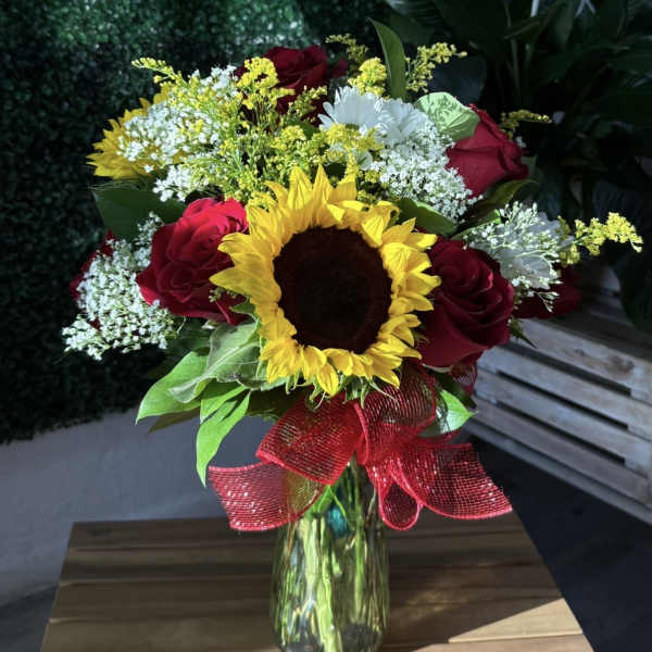 Sunflower and red rose bouquet in a glass vase with a red ribbon