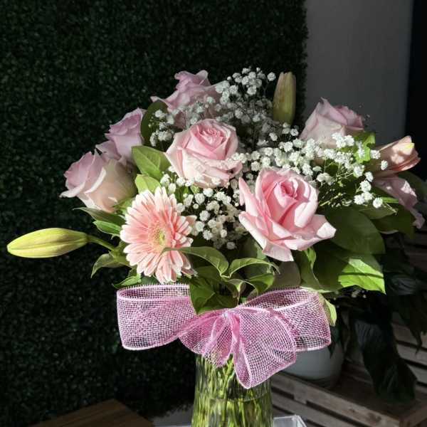 Pink roses and a gerbera daisy in a glass vase with a pink bow