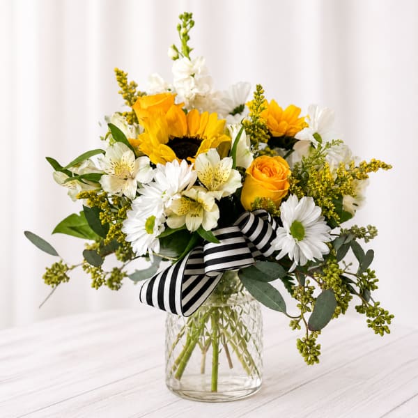 Sunflower and white daisy bouquet in a glass vase with a striped ribbon