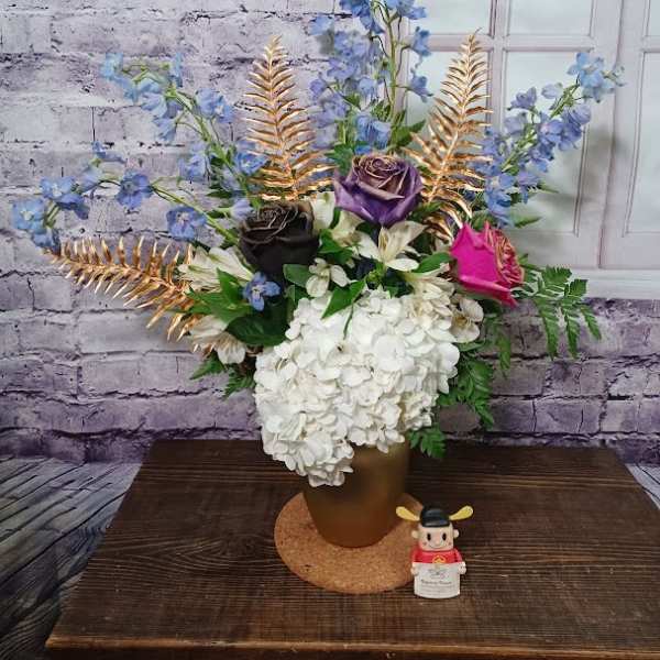 Arrangement of hydrangeas, roses, and blue flowers in a gold vase