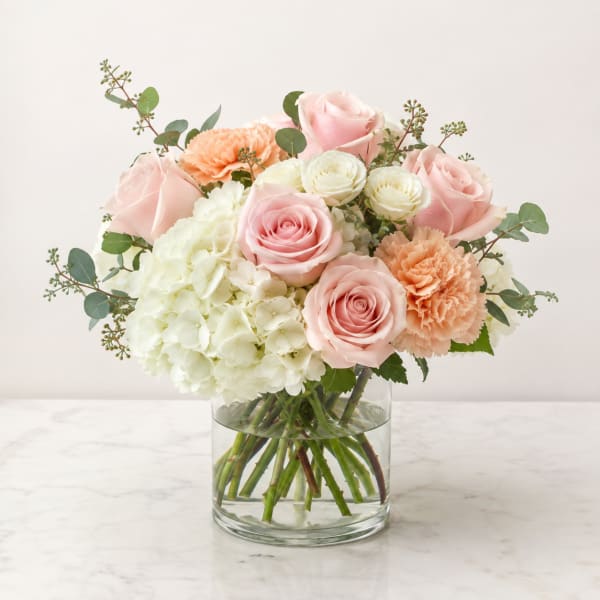 Pink roses, white hydrangea, and peach carnations in a clear glass vase